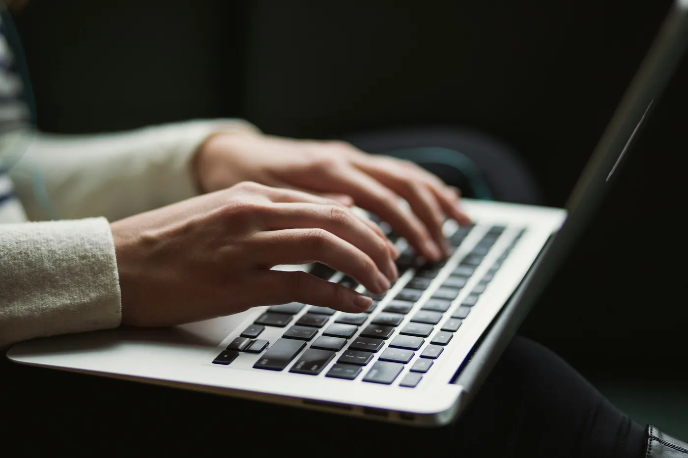 Close-up of hands typing on a laptop keyboard in low light