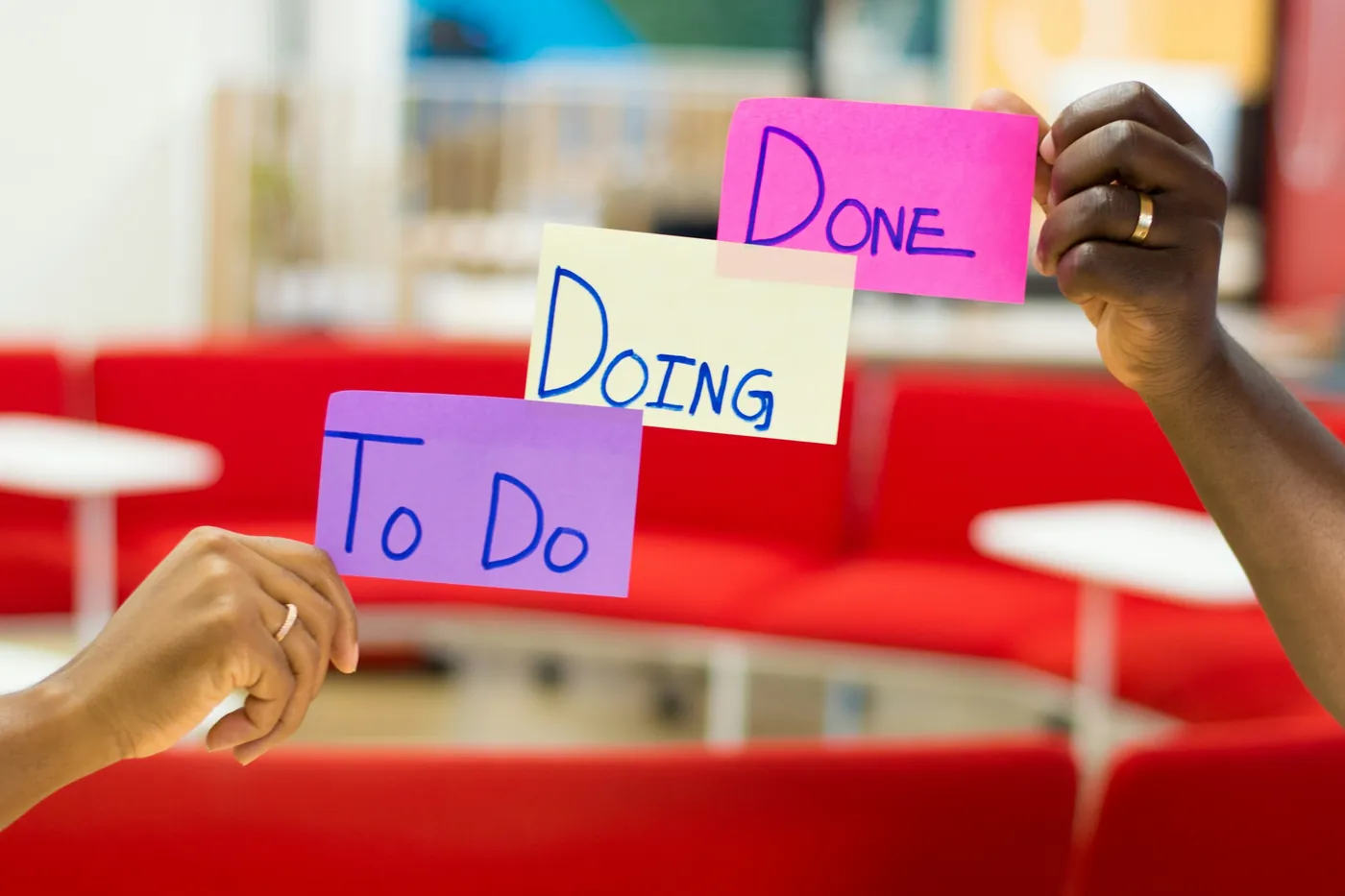 Two hands holding up sticky notes labeled To Do, Doing, and Done